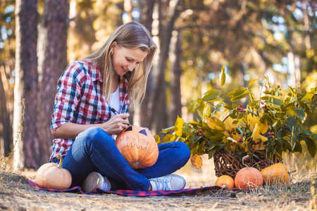 pretty woman paints a pumpkin in a pine forest.の写真素材