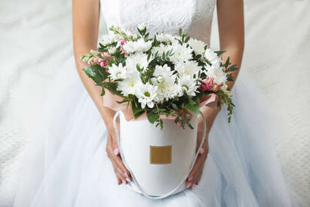 Female hands with a box of flowers on the background of a white wedding dress.の写真素材