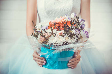 Female hands with a box of flowers on the background of a white wedding dress.の写真素材
