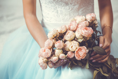 Female hands with a flowers on the background of a white wedding dress.