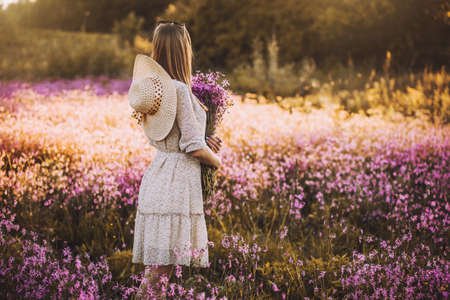 Young woman with a bouquet of wildflowers standing on a sunny blooming meadowの写真素材