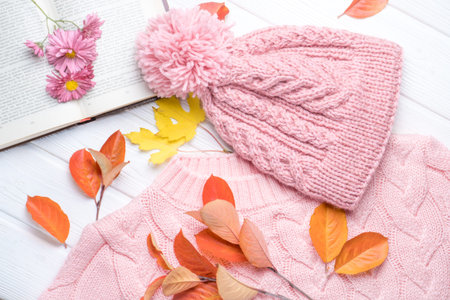 Book and a warm knitted hat and sweater, on an autumn wooden white table