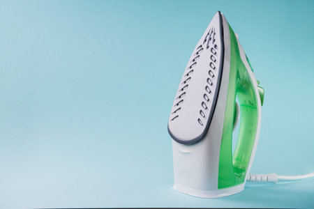 Green steam iron isolated on the blue background