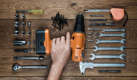 hand holding Cordless screwdriver, wrenches and tool kit on an old wooden tableの写真素材