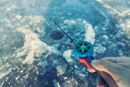man's hand holding fishing rod lowered into hole in winterの写真素材
