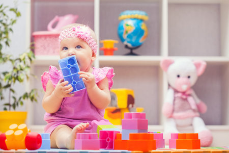 baby girl playing with colourful building blocks at home or kindergarten