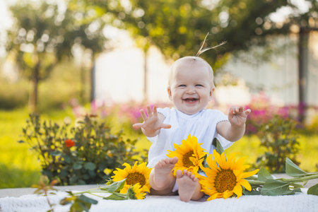 cute one year old baby girl in a blooming garden with a bouquet of sunflowersの写真素材