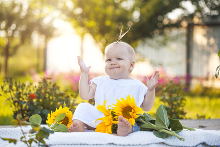 cute one year old baby girl in a blooming garden with a bouquet of sunflowersの写真素材