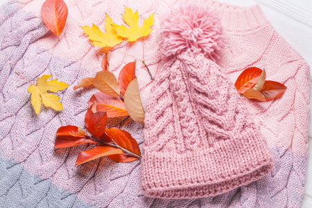 warm knitted hat and sweater, on an autumn wooden white table. Autumn background with yellow leavesの写真素材