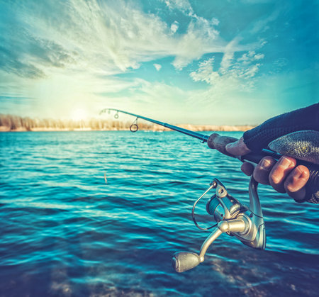 hand with spinning and reel on the summer lakeの写真素材