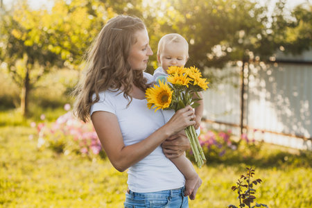 cute one year old baby girl with mom in a blooming garden with a bouquet of sunflowersの写真素材