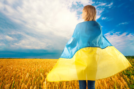 young woman with Ukrainian flag in wheat field. waving national flag praying for peace. Happy girl celebrating Independence Day.の写真素材