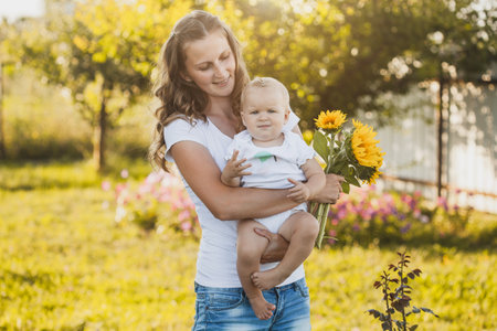 cute one year old baby girl with mom in a blooming garden with a bouquet of sunflowersの写真素材