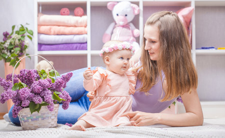 Happy mother with a little daughter with a bouquet of lilacs in the childrens roomの写真素材