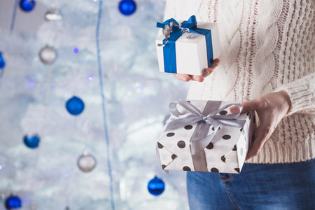 woman in white sweater and jeans in front of Christmas tree with presentの写真素材