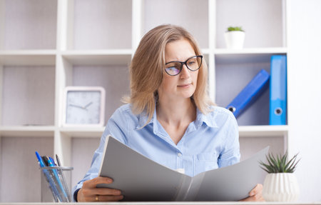 Young beautiful businesswoman sitting in a chair and reading documents at her working place. office work conceptの写真素材