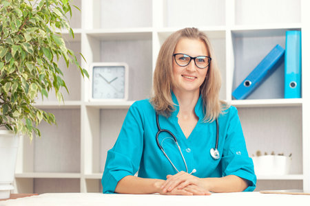 Young woman doctor in a turquoise coat in a clinical office. Health care concept.の写真素材