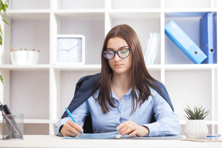 Young beautiful businesswoman sitting in a chair and reading documents at her working place. office work conceptの写真素材