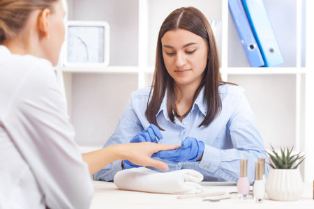 Beautician puts nails on the client. woman in a nail salon getting a manicure by a cosmetologist with a nail file.の写真素材
