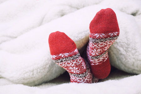 Christmas red warm socks covered with blanket on white bed. Happy moments of winter holiday....