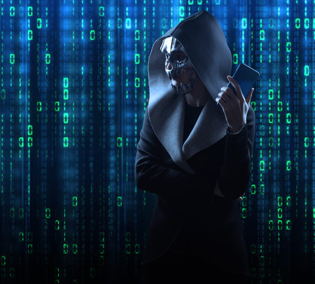 a hacker in a scary mask and hood stands against the background of a digital binary code. Hacking the Internet.の写真素材