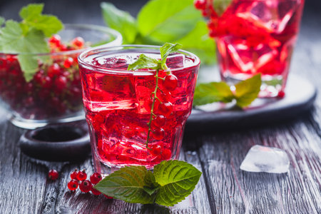 Red currant cocktail with ice and fresh mint on a black wooden tableの写真素材