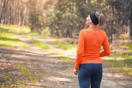 young girl on a morning run in a sunny pine forest. back view. cardio workout and healthy lifestyleの写真素材
