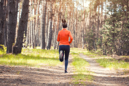young girl on a morning run in a sunny pine forest. back view. cardio workout and healthy lifestyleの写真素材
