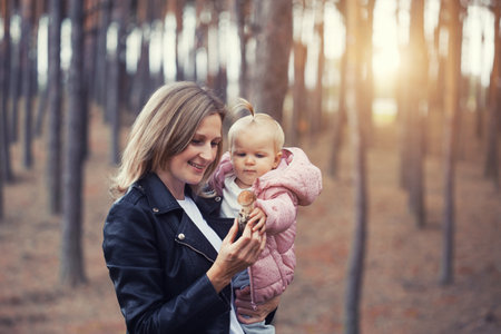 mom and little baby daughter are walking in a pine forest. mother carries her baby on her neckの写真素材