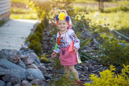 cute cheerful little girl in national Ukrainian clothes in a sunny summer gardenの写真素材