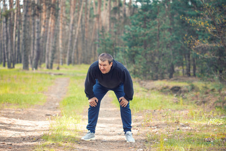 tired overweight man on a morning run in a sunny pine forest. cardio workout and healthy lifestyleの写真素材