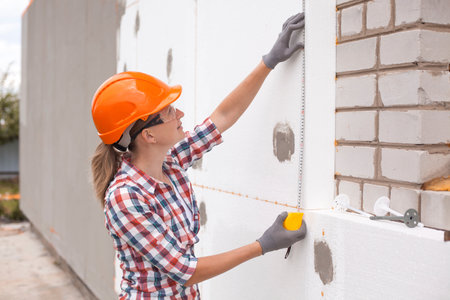 Insulation of the house with polyfoam. The woman worker is checking with the construction level the accuracy of the installation of polystyrene board on the facade.の写真素材