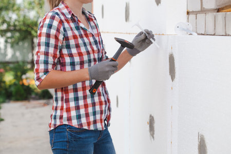 Insulation of the house with polyfoam. The woman worker is checking with the construction level the accuracy of the installation of polystyrene board on the facade.の写真素材