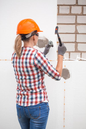 Insulation of the house with polyfoam. The woman worker is checking with the construction level the accuracy of the installation of polystyrene board on the facade.の写真素材
