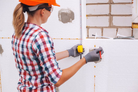 Insulation of the house with polyfoam. The woman worker is checking with the construction level the accuracy of the installation of polystyrene board on the facade.の写真素材