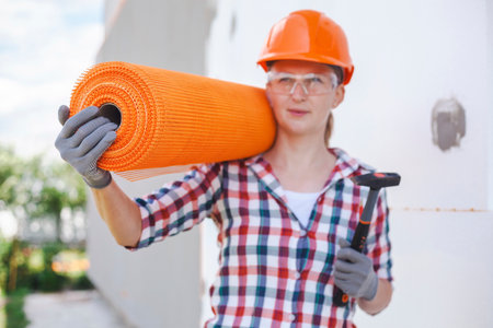 The woman worker with rolls of reinforcing fiberglass. Insulation of the house with polyfoam board on the facadeの写真素材