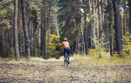 Happy woman cyclist, in a helmet, rides in the forest on a mountain bike. Adventure travel.の写真素材