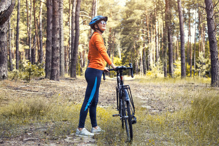 Happy woman cyclist, in a helmet, rides in the forest on a mountain bike. Adventure travel.の写真素材