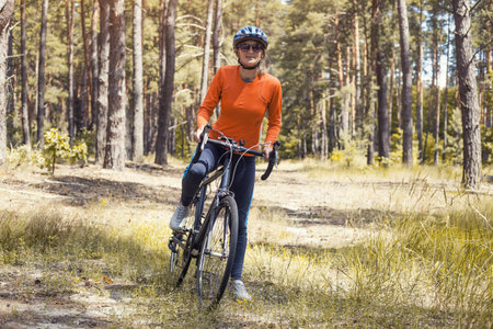Happy woman cyclist, in a helmet, rides in the forest on a mountain bike. Adventure travel.の写真素材
