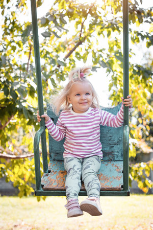 little girl rides on a swing in a beautiful summer garden. Active summer holidays for children.の写真素材
