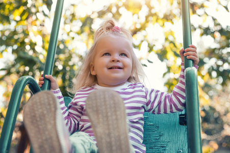 little girl rides on a swing in a beautiful summer garden. Active summer holidays for children.の写真素材