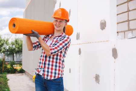 The woman worker with rolls of reinforcing fiberglass. Insulation of the house with polyfoam board on the facadeの写真素材