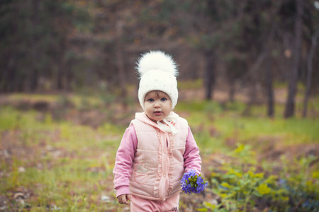 blue-eyed girl baby in a white hat walks in the spring forestの写真素材