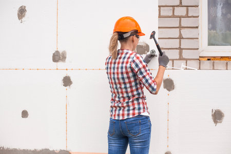 Insulation of the house with polyfoam. The woman worker is checking with the construction level the accuracy of the installation of polystyrene board on the facade.の写真素材