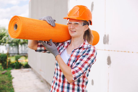 The woman worker with rolls of reinforcing fiberglass. Insulation of the house with polyfoam board on the facadeの写真素材