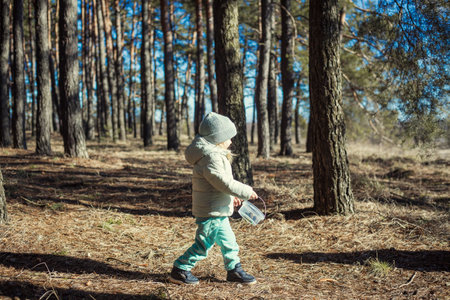 blue-eyed girl baby in a green hat walks in the pine spring forestの写真素材