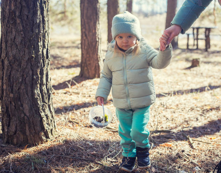 blue-eyed girl baby in a green hat walks in the pine spring forestの写真素材