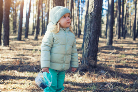 blue-eyed girl baby in a green hat walks in the pine spring forestの写真素材
