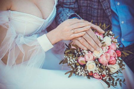 Hands of bride and groom with rings on wedding bouquet. Marriage concept.の写真素材