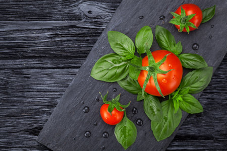 ripe fresh red tomatoes with basil leaves on a black slate board. Flat layの写真素材